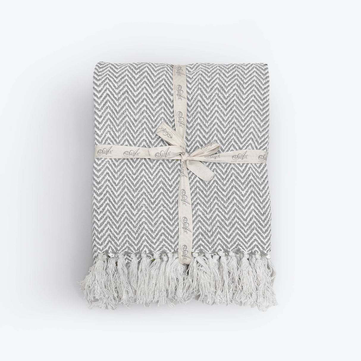 Grey and white chevron patterned throw blanket with tassels on a light gray background