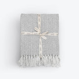 Grey and white chevron patterned throw blanket with tassels on a light gray background