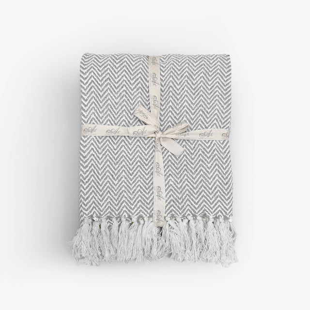 Grey and white chevron patterned throw blanket with tassels on a light gray background