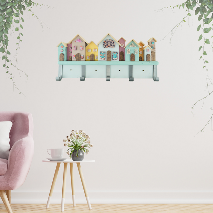 A handcrafted coat hook rack with a series of pastel-colored houses mounted on a wall, featuring five coat hooks beneath the houses.