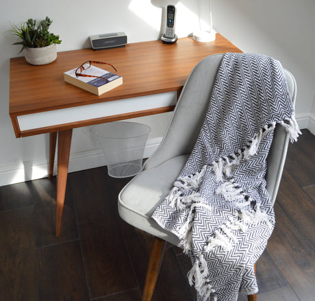 Wooden desk with a chair draped with a black and white patterned towel, in a home office setting.