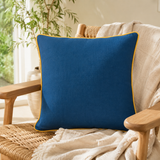 Plain deep blue linen cushion cover with mustard piping styled on a cream sofa.