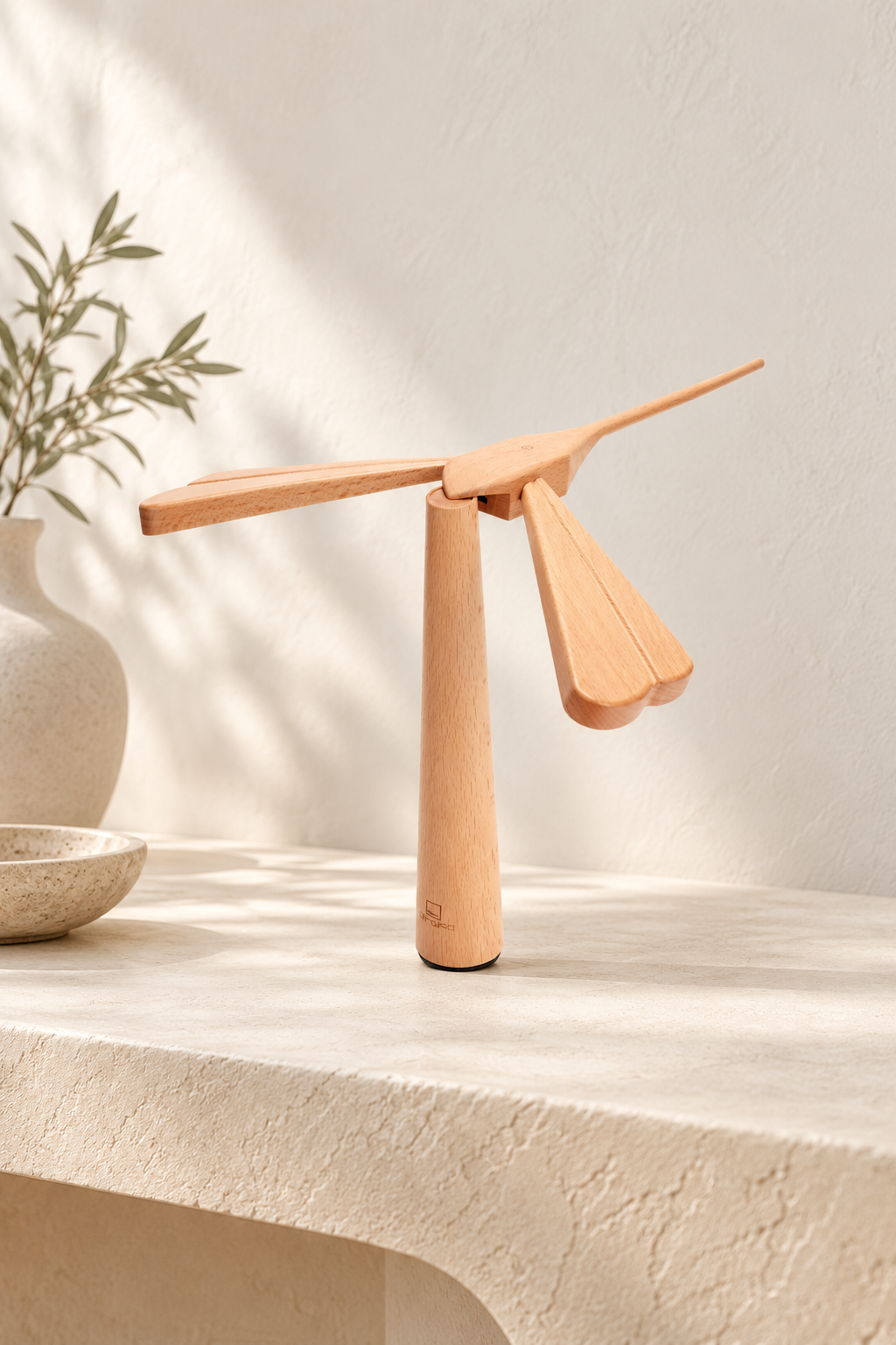 Maple Dragonflight Balance Light resting on its cylindrical wooden stand on an ivory console, with four outstretched wings and a raised tail.