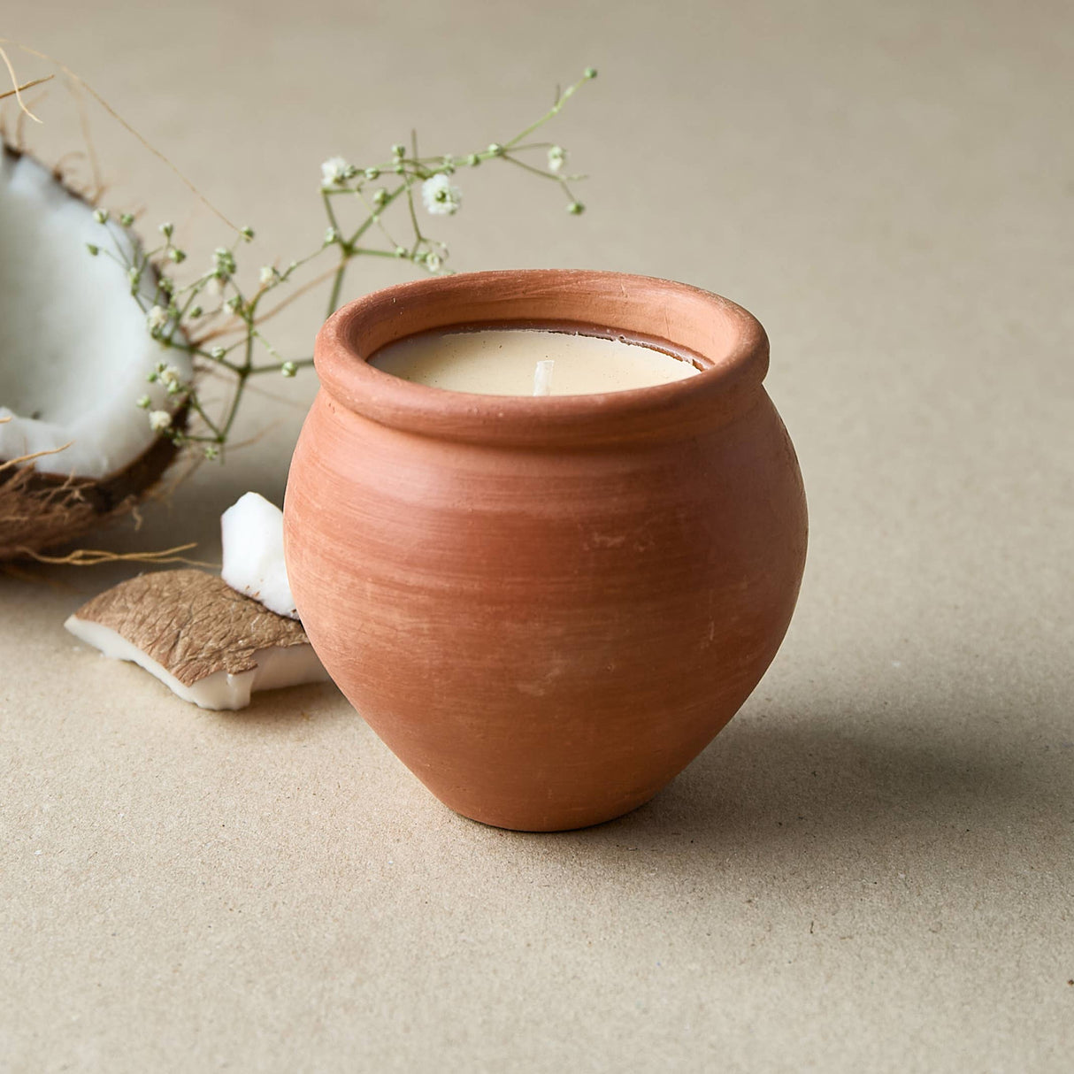 Terracotta pot with a candle on a beige surface with a coconut and flowers.