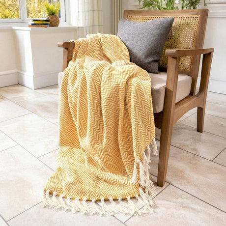 Yellow textured blanket draped over a wooden chair with a grey pillow on a tiled floor.