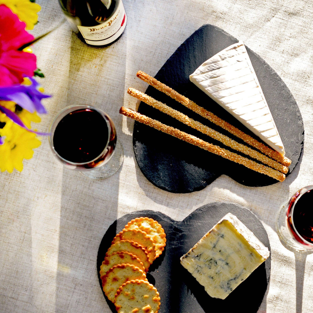 Plates of cheese and crackers with glasses of red wine on a tablecloth.