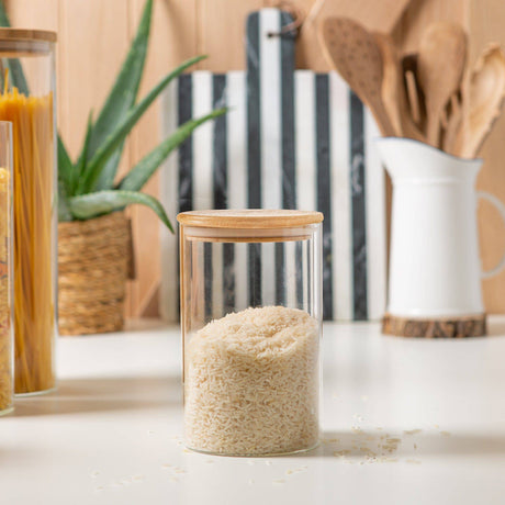 Glass container with rice on a kitchen counter with wooden utensils and a plant in the background.