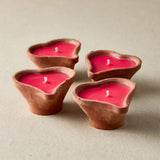 Four heart-shaped clay candles with red wax on a beige background