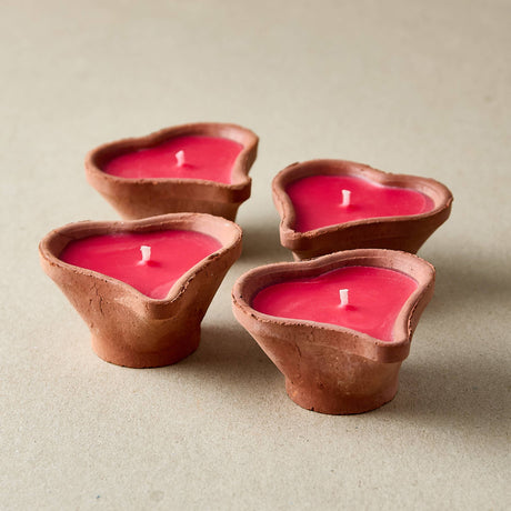Four heart-shaped clay candles with red wax on a beige background