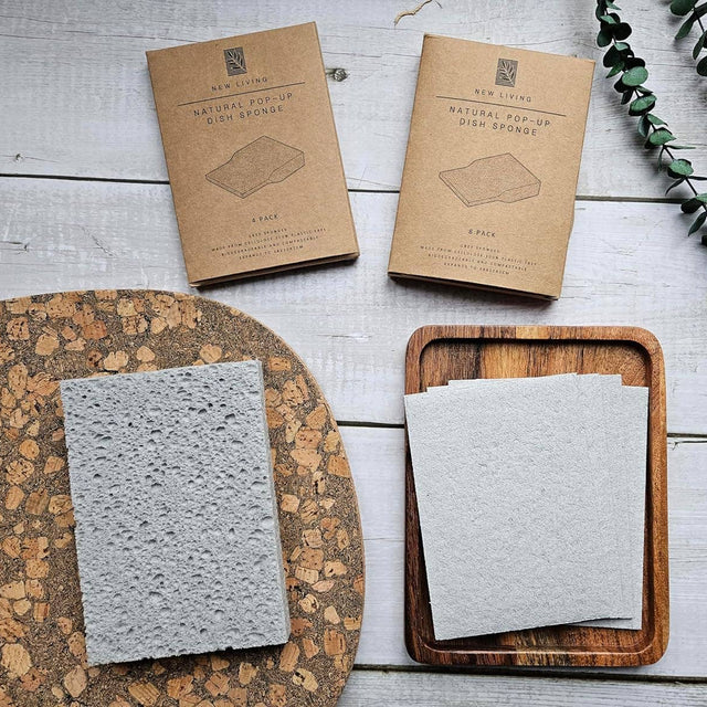  natural pop-up dish sponges on a wooden tray with packaging and eucalyptus leaves on a wooden surface.