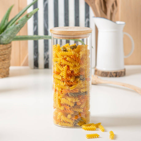 Glass jar with wooden lid filled with pasta on a light surface.