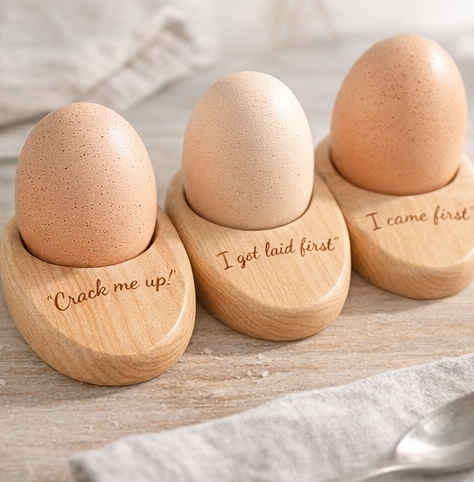 Three wooden egg holders with humorous engravings on a wooden surface.