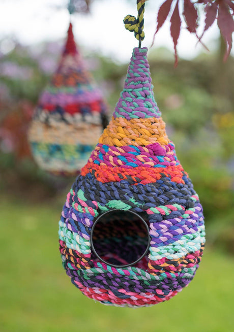 Colorful woven birdhouse hanging outdoors with a blurred garden background