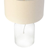 Lamp with beige fabric shade and clear glass base on a white background