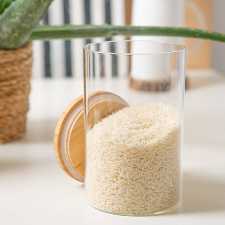 Clear glass container filled with rice on a light surface with a plant in the background
