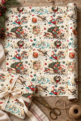 Festive sheep paper unrolled beside a cream-ribbon gift, twine and brass scissors.