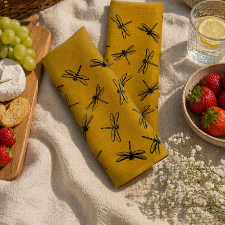 Yellow linen tea towels with black dragonfly pattern on a picnic setup with fruits, bread.