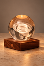 Saturn Amber Crystal Light on a square walnut base against a neutral studio backdrop, showing the illuminated ringed planet inside the clear sphere.