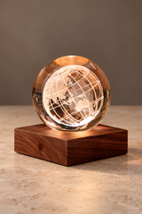 World Globe Amber Crystal Light glowing on a square walnut base against a neutral studio backdrop, with engraved continents and grid lines.