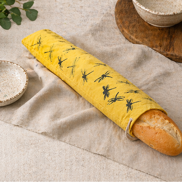 hand printed Yellow dragonfly patterned linen bread bag used to cover a loaf of bread on a wooden board and table.