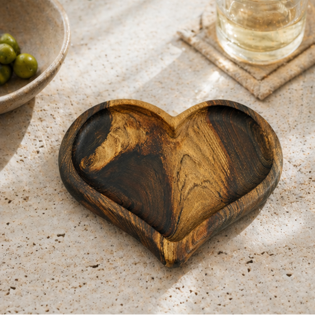 Heart-shaped wooden coaster on a marble surface with a glass of water and a plant.