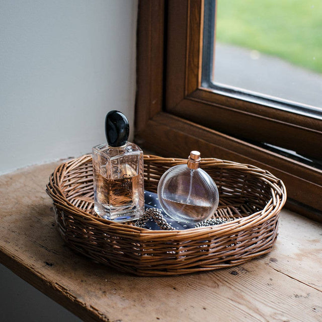 Two perfume bottles on a woven tray by a window