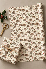 Hedgehog Winter Foliage wrapping paper unrolled on a table beside a wrapped gift, twine and scissors.