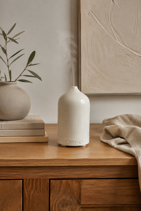 White ceramic diffuser on a wooden surface with a plant and books in the background