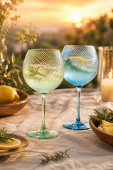Two colorful gin glasses on a table with sunset background