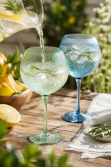 Two gin glasses being filled with a clear liquid on a wooden table outdoors.