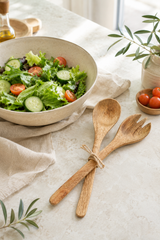 Salad bowl with mango wood, wooden utensils on a table with a plant in the background