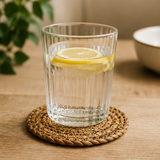 Clear glass of water with a lemon slice on a woven coaster on a wooden surface.