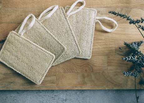 Three natural fiber scrubbies on a wooden surface with lavender flowers.