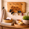 Wooden key holder with keys on a wall above a wooden surface with a basket, books, and plants.