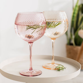 Two pink and clear wine glasses with herbs on a white surface.