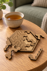 Pocket Hex oak-veneered puzzle with loose pieces on an oak table beside a ceramic cup of tea.