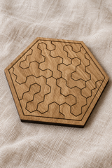 Close-up of the assembled Pocket Hex puzzle on linen, showing geometric pieces, oak veneer and a thin dark edge.