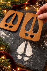 Lifting a wooden reindeer hoof stencil to reveal the cloven hoof and dewclaw print beneath.