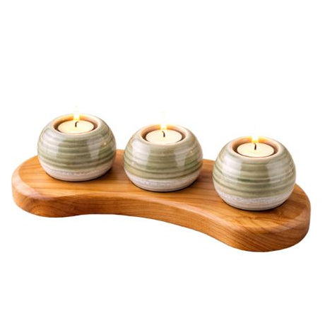 Three ceramic candle holders on a wooden base with white candles inside, on a white background.