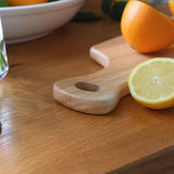 Close-up of the rounded wooden handle and hanging hole on the 34 × 16cm rubberwood board, beside a lemon half and sliced orange.