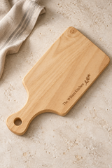 34 × 16cm rubberwood handled board engraved “The Wilson Kitchen” with a leafy motif along one edge, viewed from above on a pale surface.