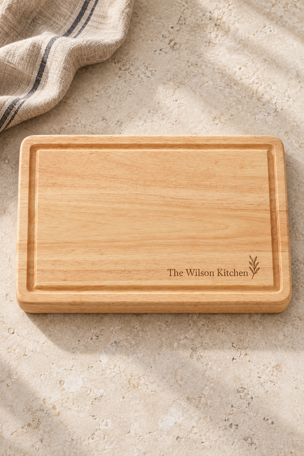 30 × 20cm rubberwood butcher’s block engraved “The Wilson Kitchen” with a small leafy motif, lying on a pale kitchen worktop.