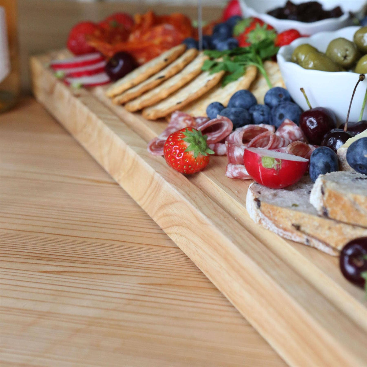 Close-up of the 60 × 40cm rubberwood butcher’s block serving bread, salami, strawberries, blueberries and olives.