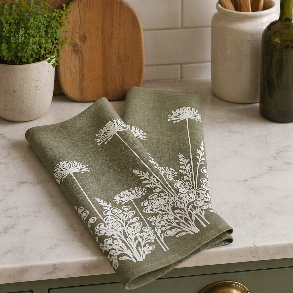 sage Green towel with hand printed white floral pattern on a kitchen counter with wooden cutting boards and utensils.