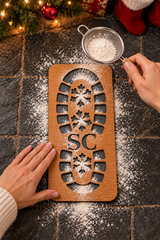 Sifting white powder through a Santa boot stencil laid flat to create a Christmas Eve footprint.
