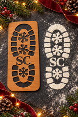 Wooden Santa boot stencil beside its matching white footprint, showing the snowflake tread and SC detail.