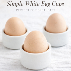 Three brown eggs in white ceramic cups on a white textured surface with text 'Simple White Egg Cups Perfect for Breakfast'.