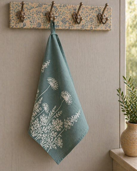 Linen tea towel with floral pattern hanging on a wooden hook rack against a neutral wall.