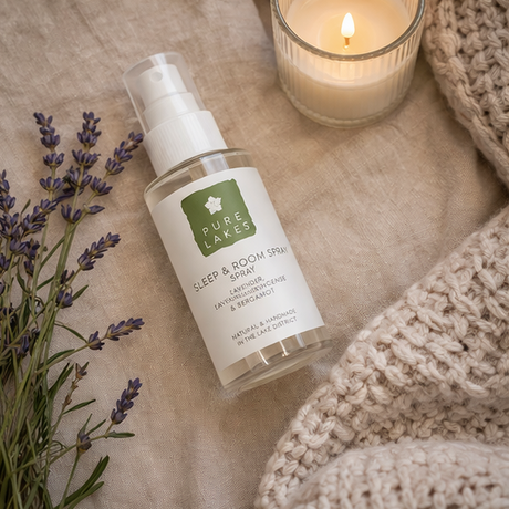 Bottle of Pure Lakes Sleep & Room Spray with lavender and a candle on a textured surface