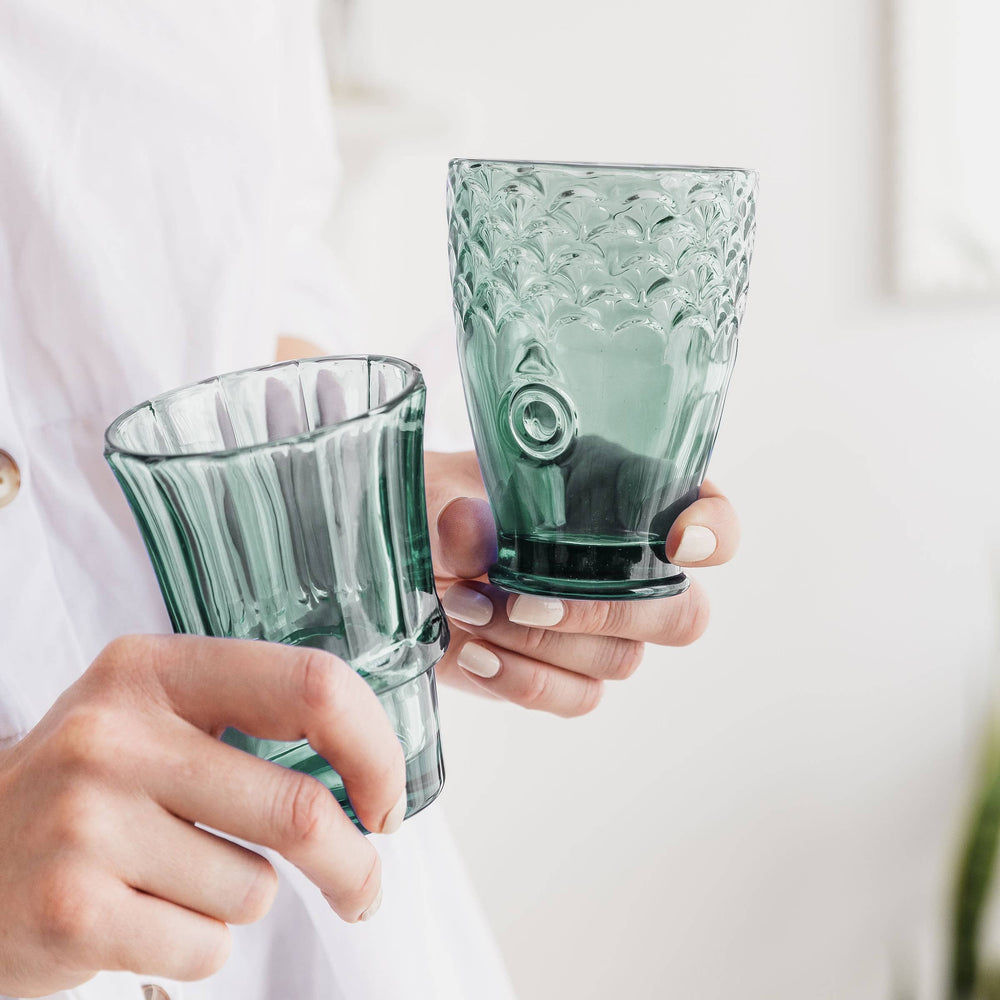 hands holding green glass stacking  tumblers against a light background